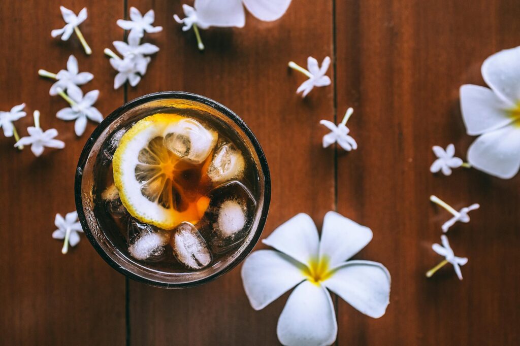 composition with glass of fresh drink and tropical white flowers